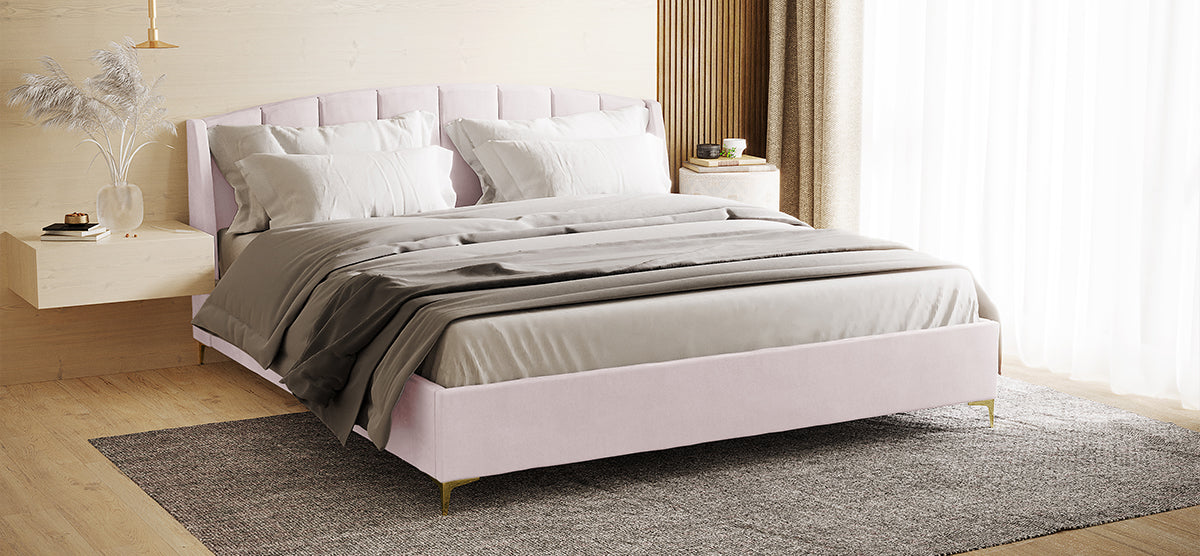 Modern bedroom corner with a blush-pink upholstered platform bed, neutral bedding, a floating nightstand with pampas grass, a round side table, and a gray area rug.