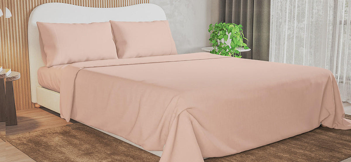 A minimalist bedroom with a bed featuring a pale-peach upholstered headboard, matching sheets, a wooden nightstand with a lamp, books, and a potted plant by the window.