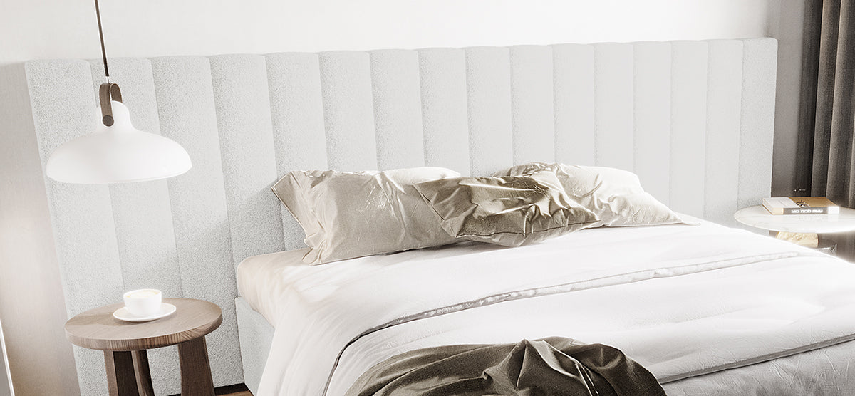 Modern minimalist bedroom with a white-linen bed, upholstered headboard, two pillows, dark wood table with coffee cup, light wood table with book, and a white hanging lamp.