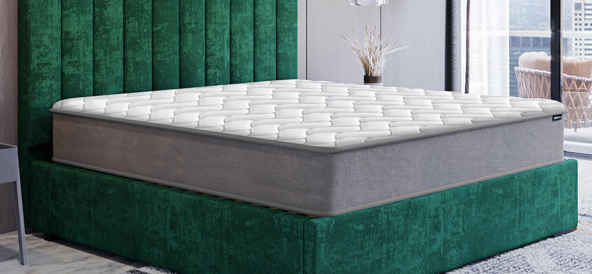 Modern bedroom featuring a thick, gray-sided mattress with a white quilted top on a green upholstered bed base, complemented by simple decor and a cityscape view.