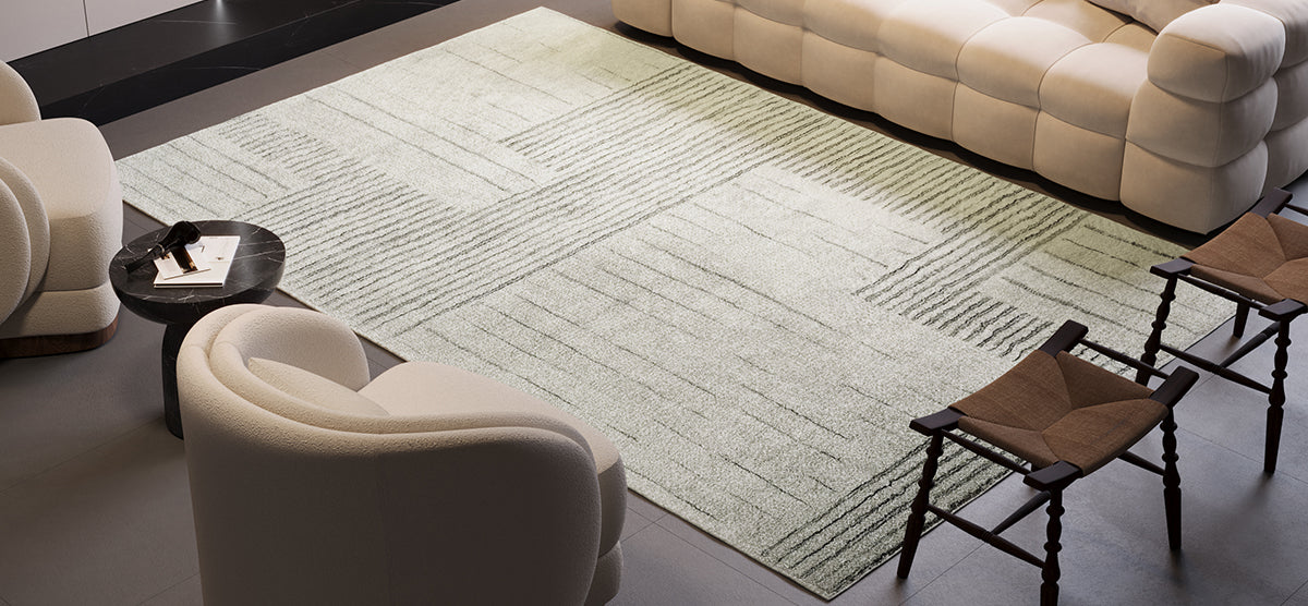 A modern living-room vignette featuring a muted geometric-pattern rug, rounded white bouclé chairs, a tufted cream sofa, black marble side table, and dark-wood stools with woven leather seats.
