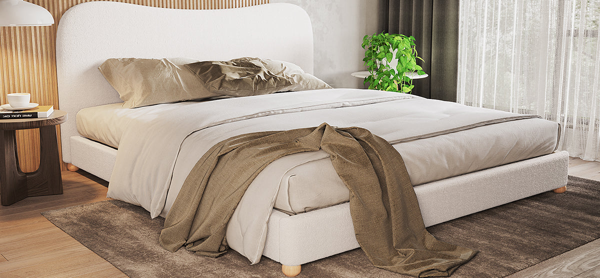 Contemporary bedroom with a low-profile upholstered bed in neutral tones, wooden side table, white lamp, potted plant, and sheer curtains, framed by wood slat and plaster walls.