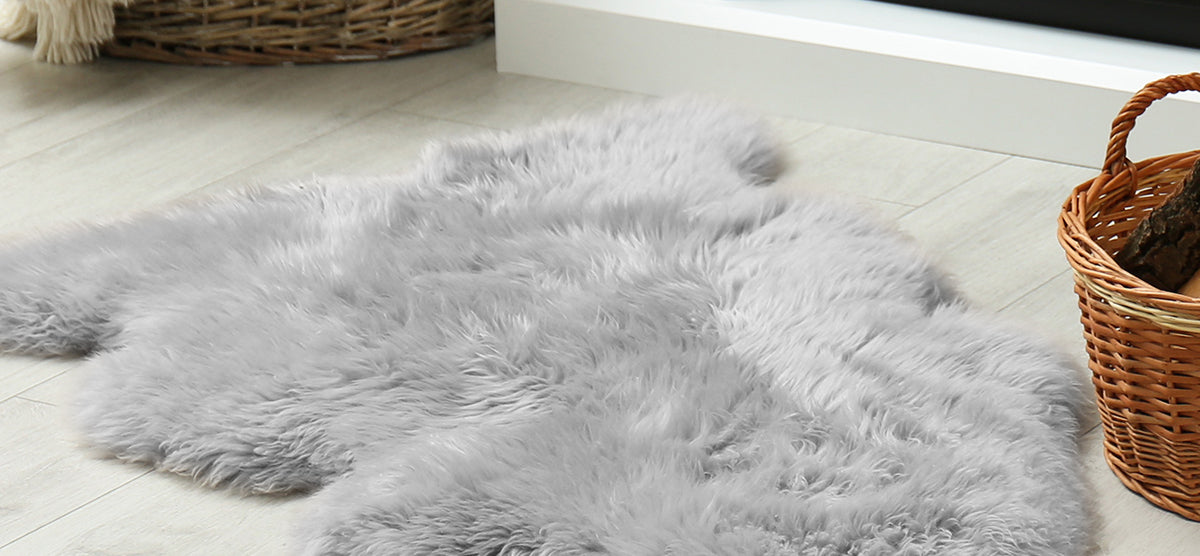 Gray faux-sheepskin rug on light wood floor, alongside a wicker basket filled with firewood, creating a cozy home-decor vignette.