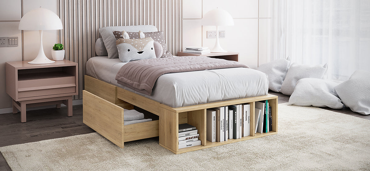 A modern bedroom corner featuring a low wooden platform bed with storage, light gray bedding, mauve-gray throw, plush animal pillow, pink bedside tables, and a cozy cushion nook by a sunlit window.