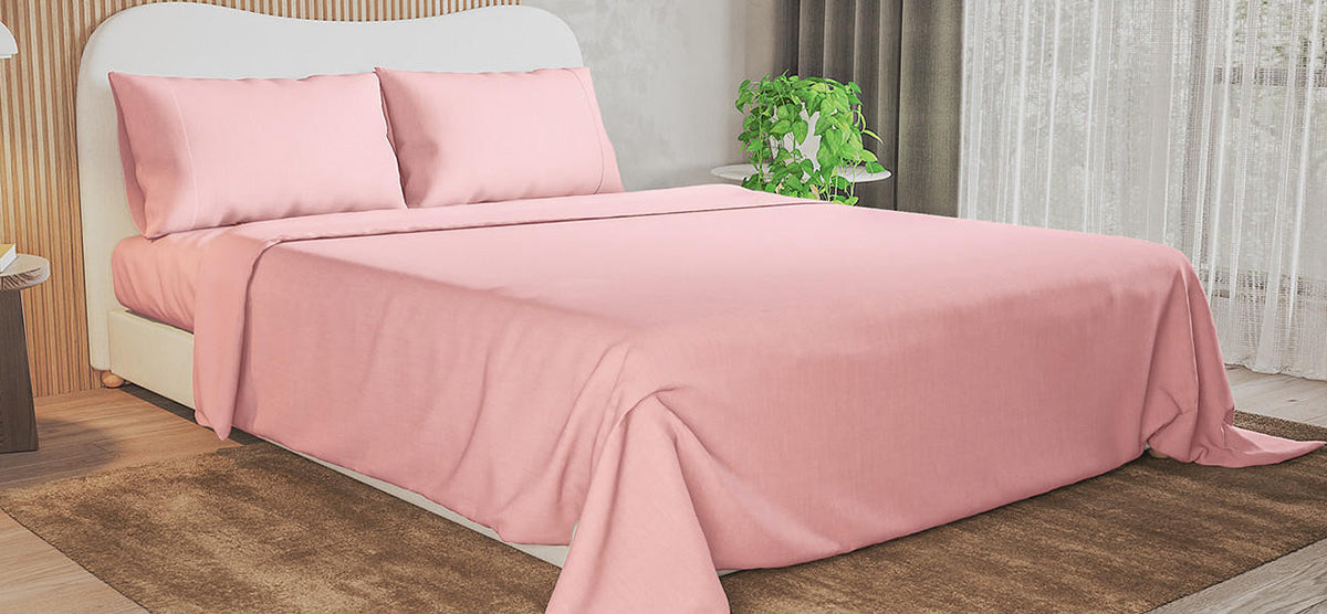 Solid-pink linens on a neatly made bed with a white curved headboard. A side table with a potted plant and light-gray curtains complement the minimalist setup.
