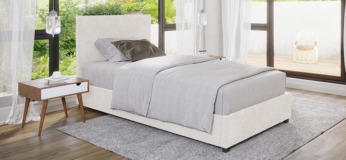 A modern bedroom with an upholstered platform bed in gray, a mid-century nightstand, sheer curtains, and a balcony with a wicker chair, creating a serene atmosphere.