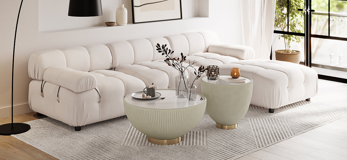Contemporary living room corner with a modular white sofa, round nesting tables with sage-green fluted bases, minimalist decor, and floor-to-ceiling windows, creating an airy, modern aesthetic.