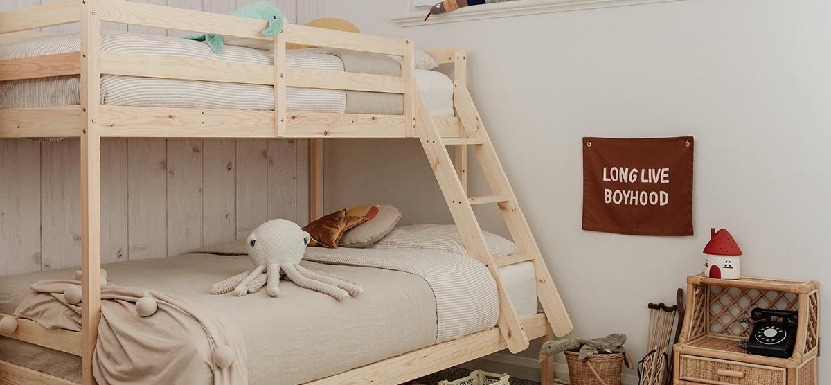 Children’s bedroom corner with a natural-wood bunk bed, featuring a white crocheted octopus plush, fabric banner saying “LONG LIVE BOYHOOD,” and a rattan shelf with decorative items.