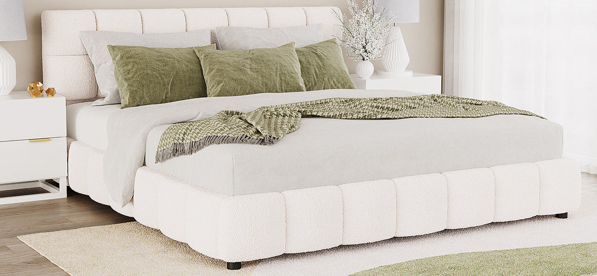 A contemporary bedroom with a cream-bouclé upholstered platform bed, light gray sheets, olive-green pillows, a green houndstooth throw, flanked by white nightstands with lamps and decorative items.