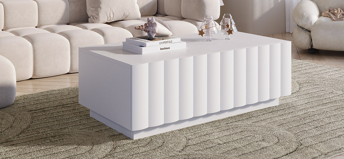 Contemporary living room with a white fluted coffee table featuring art books, a seashell, and glass lanterns, set against a beige sofa and lounge chair.