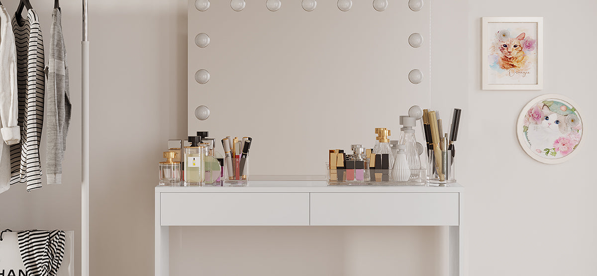 White vanity table with Hollywood-style lit mirror, clear organizers for beauty products. Nearby, a clothing rack with striped shirts, and cat-themed watercolor paintings on the wall.
