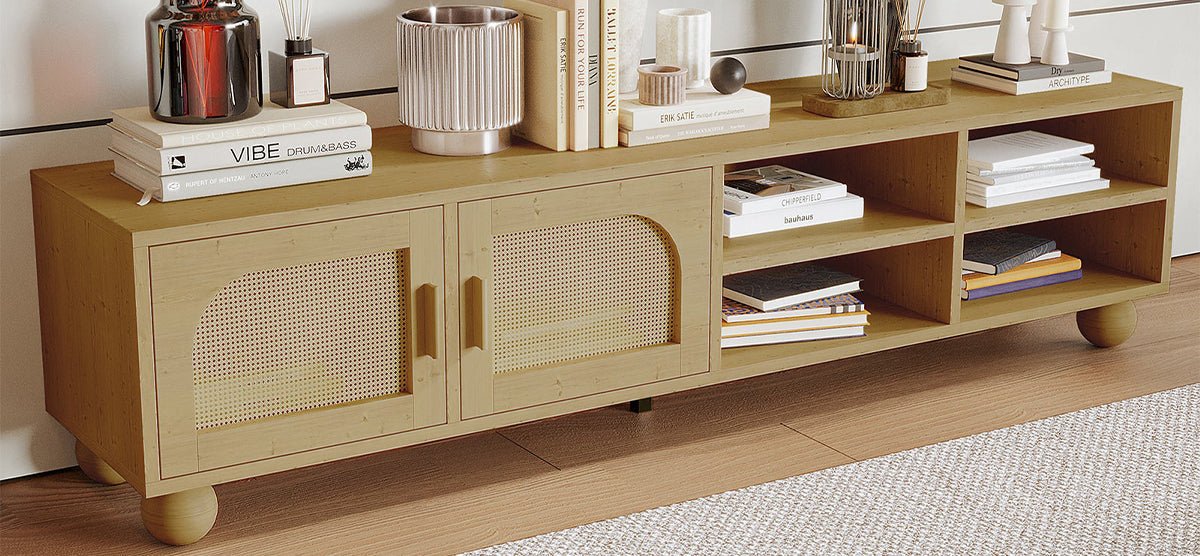 Light-wood media console with rattan-fronted doors and open shelves, adorned with decorative vases, books, and sculptures; resting on ball-shaped feet beside a woven rug.