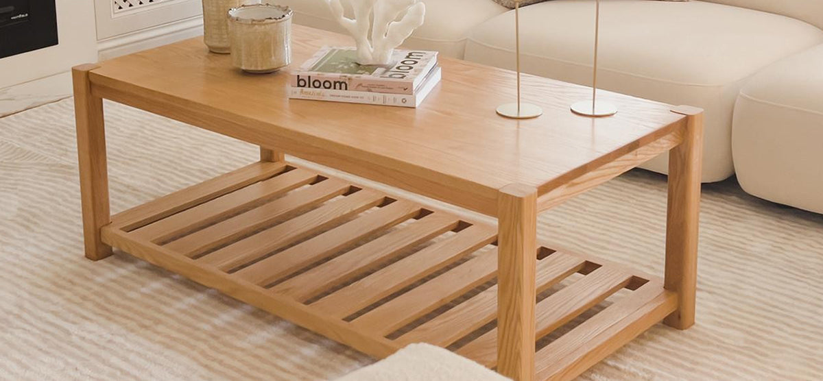 A modern living room setup featuring a rectangular wooden coffee table with a slatted shelf, adorned with books, a coral-like ornament, and candle holders, on a striped rug.