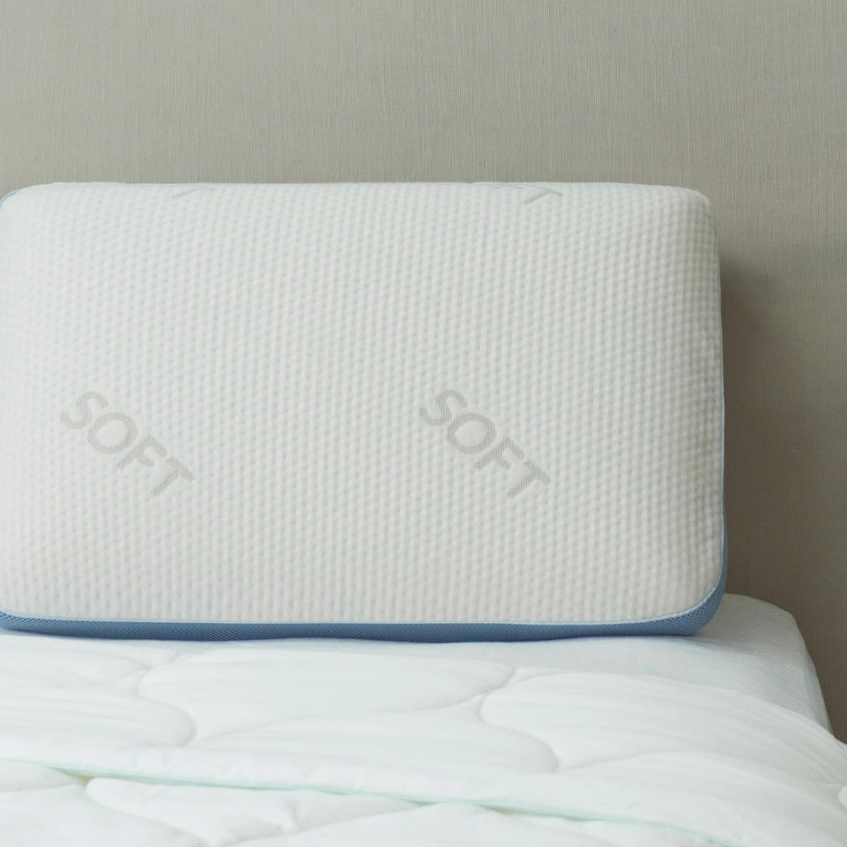 Signature memory foam pillow, Soft, with blue gusset trim, resting on a bed against a headboard