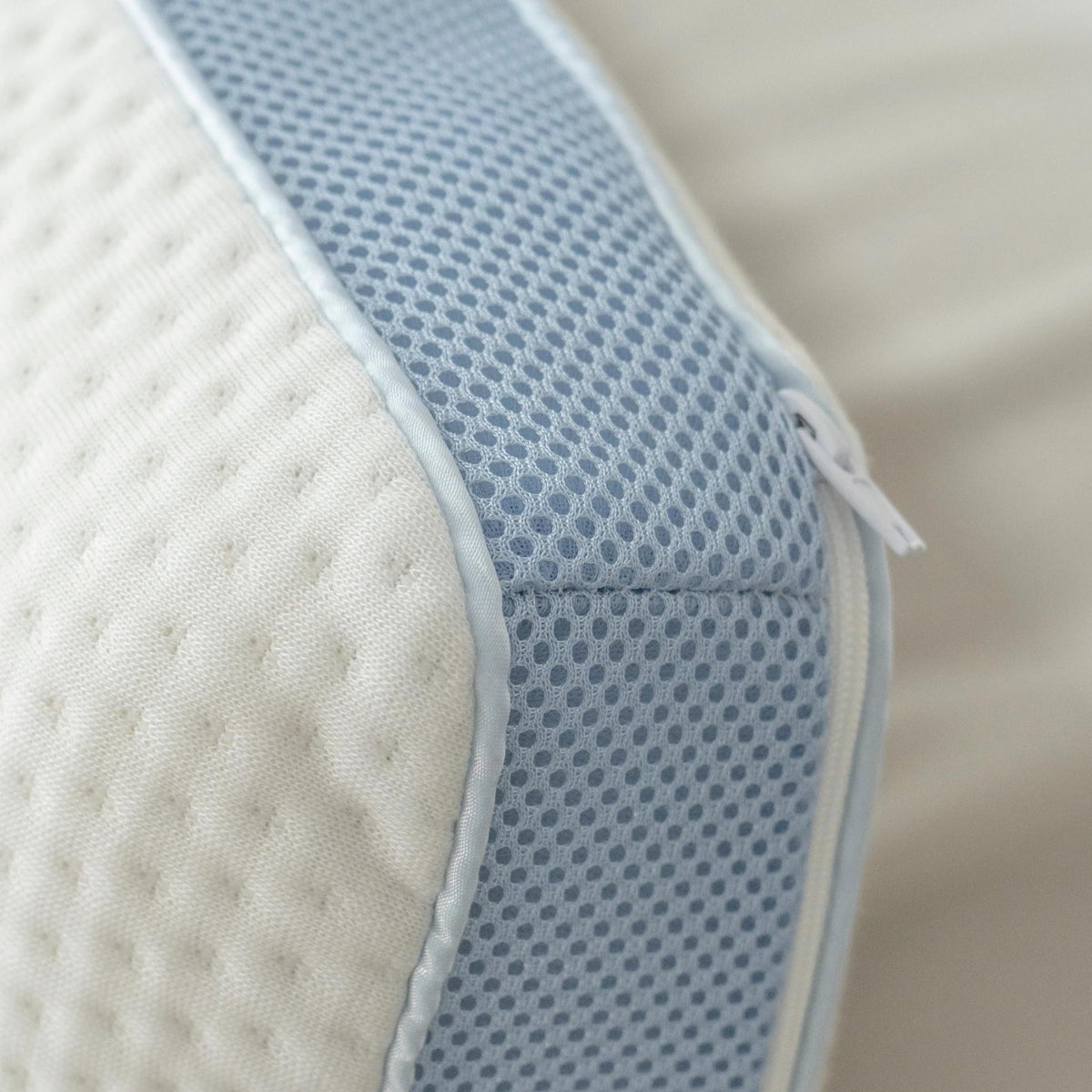 Extreme close-up of the pillow's blue mesh gusset side panel and zip pull