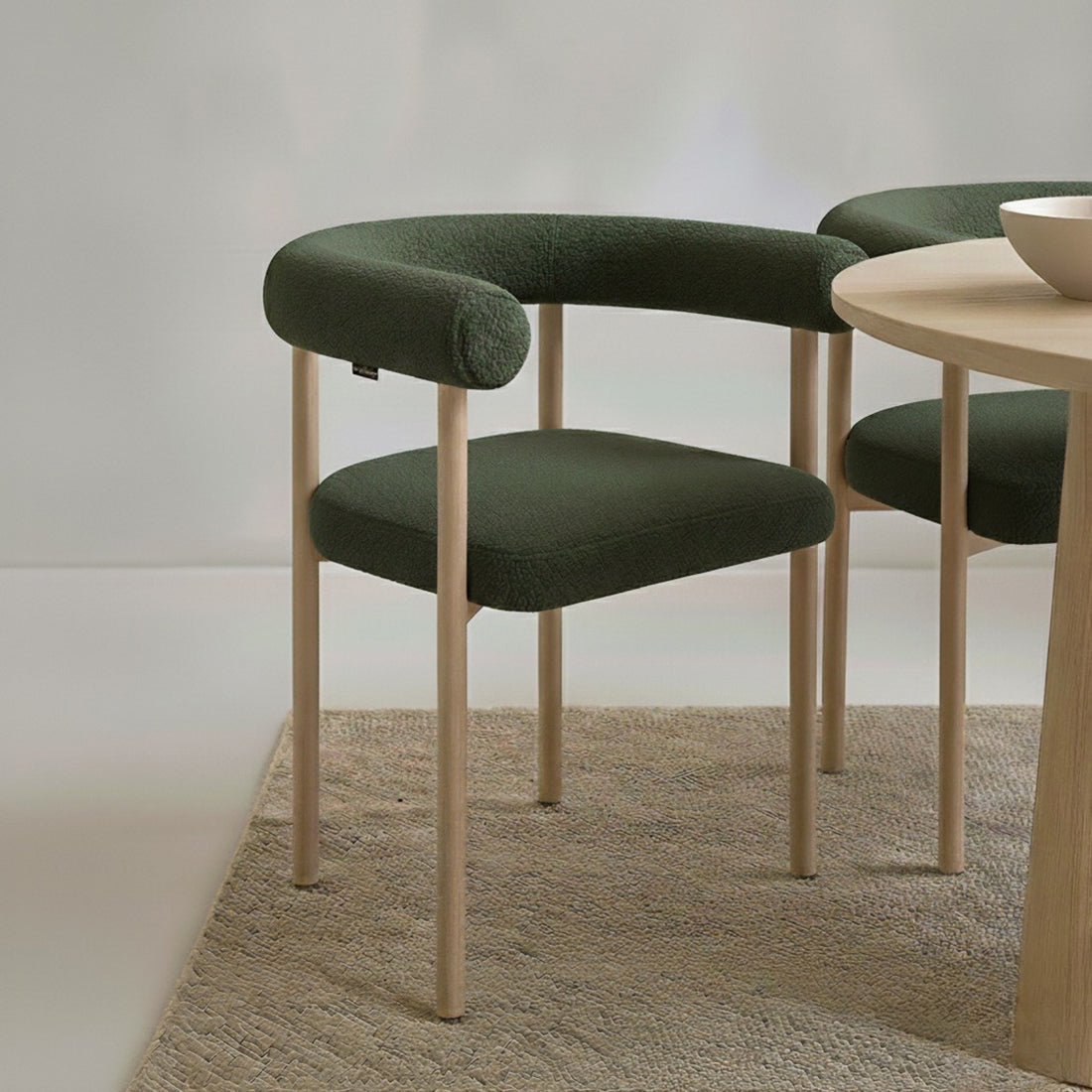 Ohio Curved Boucle Dining Chair Set of 2 in Green & Oak features a forest-green upholstered U-shaped backrest, light wood frame, and legs, paired with a coordinating round table and neutral bowl.