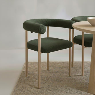 Ohio Curved Boucle Dining Chair Set of 2 in Green & Oak features a forest-green upholstered U-shaped backrest, light wood frame, and legs, paired with a coordinating round table and neutral bowl.