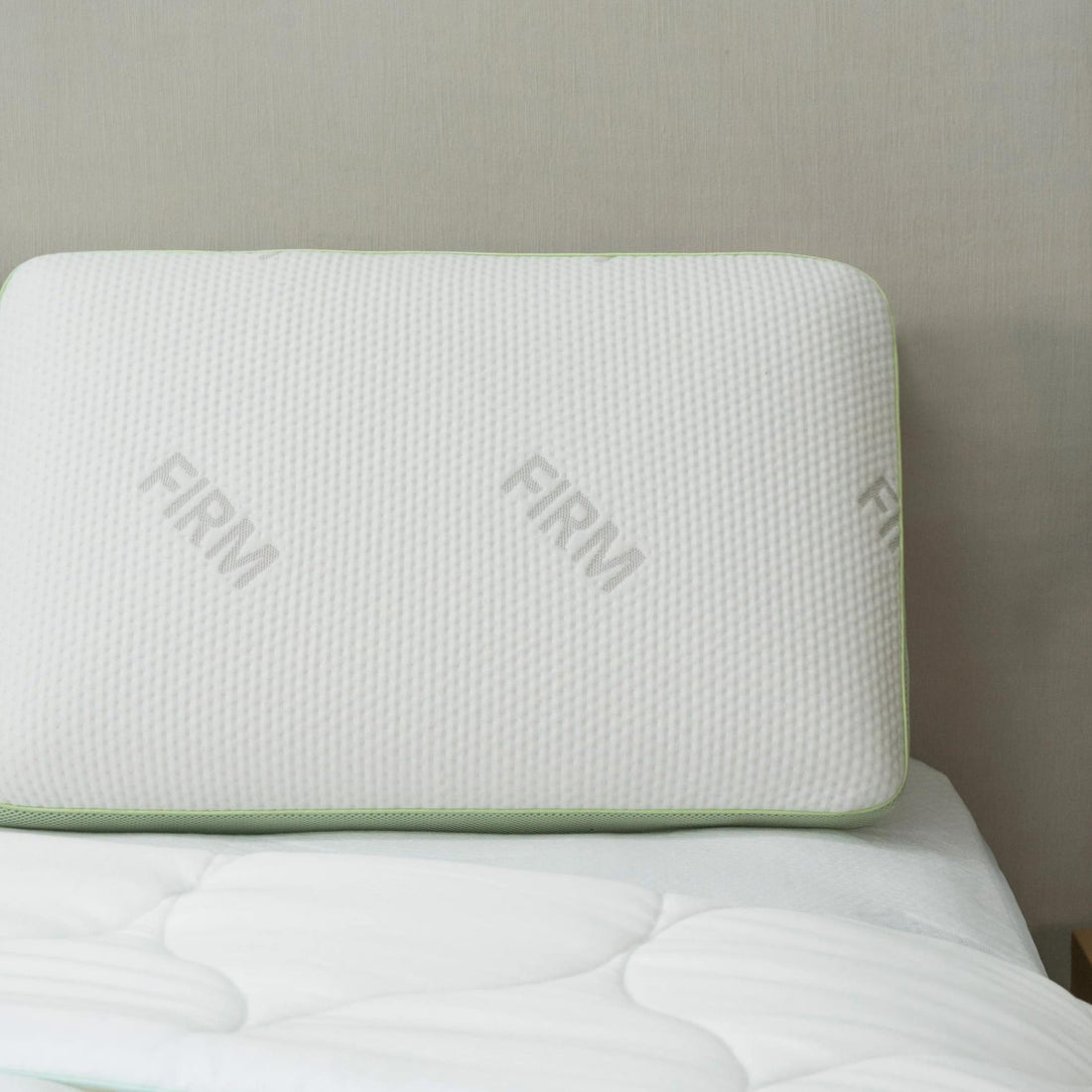 Signature memory foam pillow, Firm, with green gusset trim, resting on a bed against a headboard