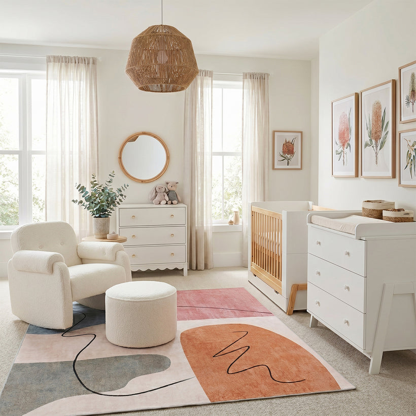Bright, modern nursery featuring a white and natural wood crib, white changing dresser, cozy boucle armchair with matching ottoman, abstract pink and terracotta area rug, woven pendant light, botanical wall art, sheer curtains, and soft neutral décor creating a warm, calming space for a baby.