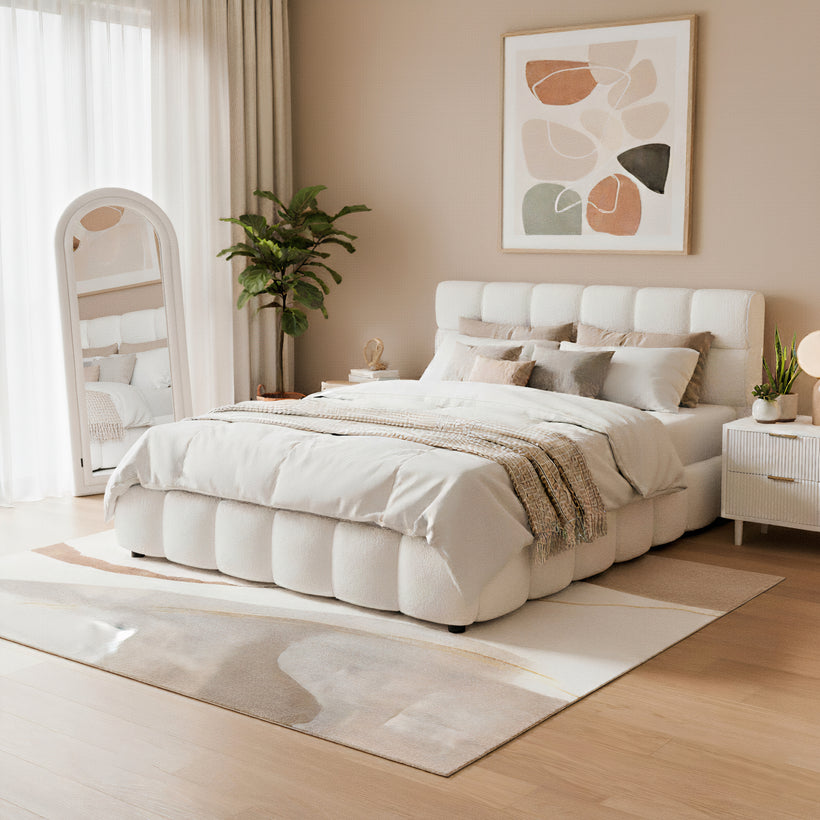 Wooden outdoor sun lounger with white cushions beside a swimming pool, paired with a small round white side table holding a refreshing orange drink. In the background, a wooden serving cart with drinks and snacks is set up on a tiled patio surrounded by greenery and a wooden privacy fence