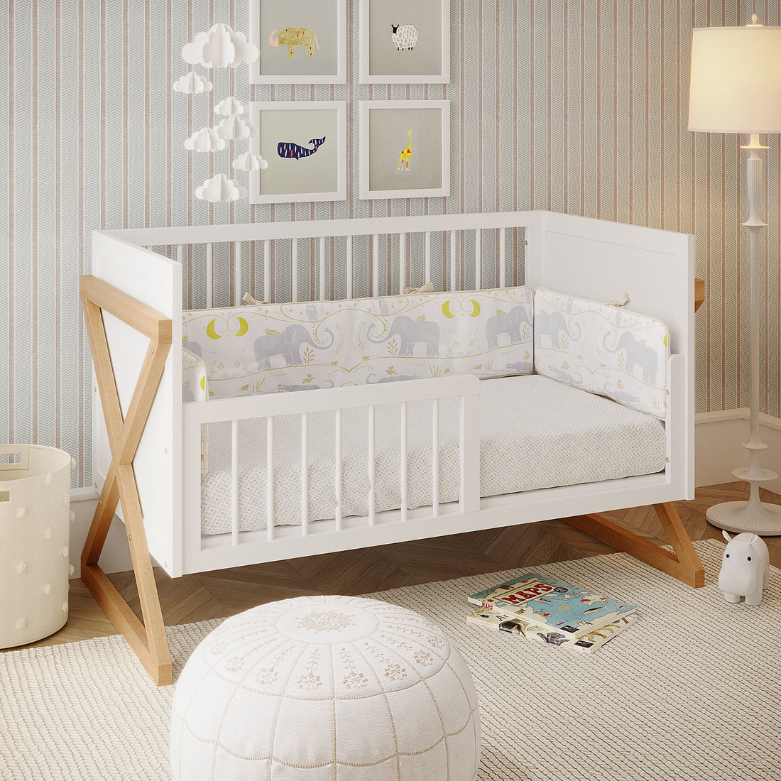 Aldwin & Melai Solid Pine Baby Cot with Rail Set in White, featuring elephant-and-moon bumper, fluffy cloud mobile, framed animal prints, woven basket, and plush pouf, embodying a Scandinavian nursery style.