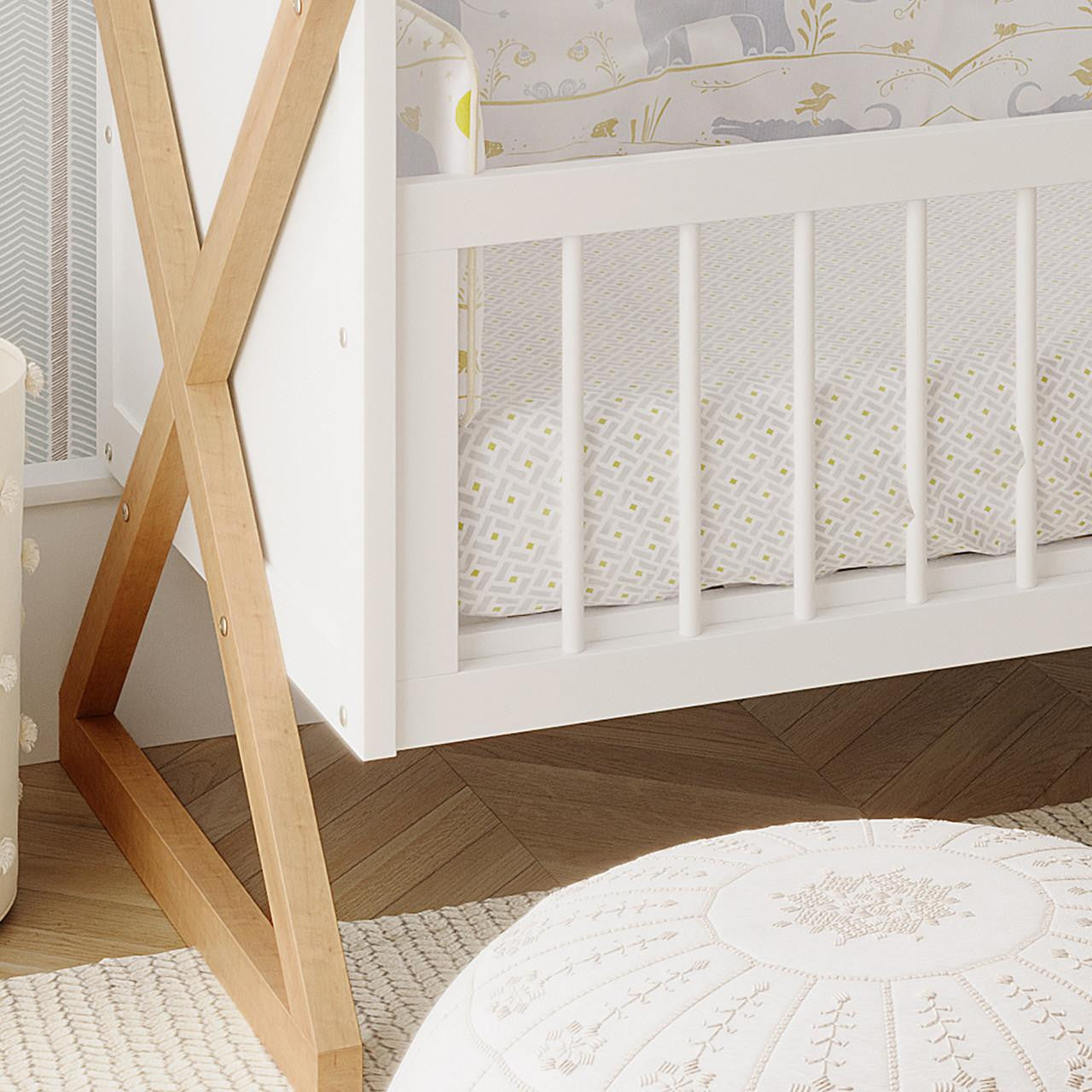 Aldwin & Melai Solid Pine Baby Cot with Convertible Rail Set White, showcasing its X-shaped wooden legs and turned slats, paired with a geometric print fitted sheet in a styled nursery corner.
