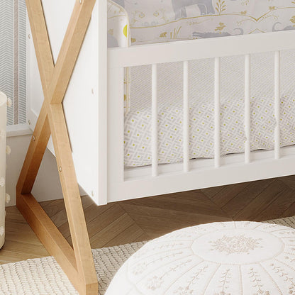 Aldwin & Melai Solid Pine Baby Cot with Convertible Rail Set White, showcasing its X-shaped wooden legs and turned slats, paired with a geometric print fitted sheet in a styled nursery corner.