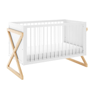 Aldwin Pine Adjustable Baby Cot - White/Natural: Modern crib with a white frame, vertical slats, and distinctive X-shaped natural wood legs, featuring an adjustable mattress height for growing babies.