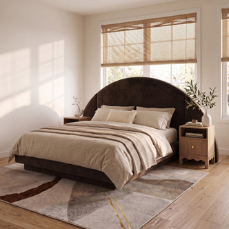 A modern neutral bedroom showcasing a dark brown velvet bed frame with an oversized half-moon headboard, styled with beige bedding and wooden nightstands on a textured abstract rug.
