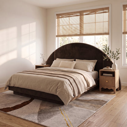 A modern neutral bedroom showcasing a dark brown velvet bed frame with an oversized half-moon headboard, styled with beige bedding and wooden nightstands on a textured abstract rug.