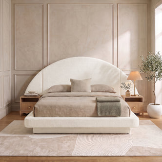 A modern neutral bedroom showcasing the Cosy Boucle Bed Frame with a statement half-moon headboard, styled with beige bedding and wooden nightstands on a textured abstract rug.