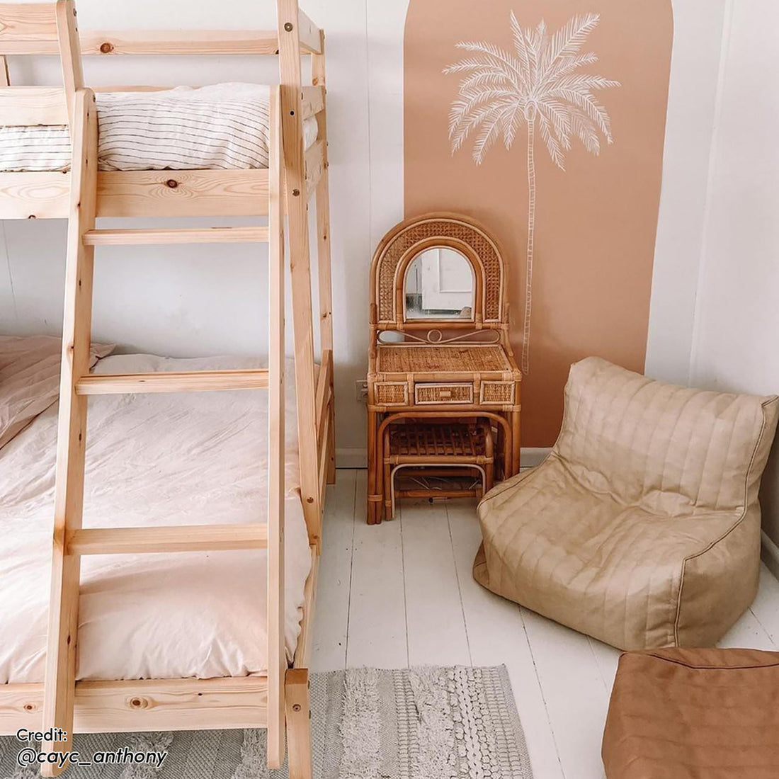 Antonia Wooden Triple Bunk Bed - Natural featuring a solid pine frame, reversible ladder, and secure guard rails, displayed in a room with a wooden ladder and palm tree drawing on the wall.
