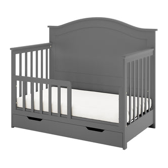 Azeem & Giro Solid Pine Convertible Cot Set in Grey, featuring a gray wooden toddler bed with partial safety rails, contoured headboard, and a pull-out storage drawer beneath the mattress.