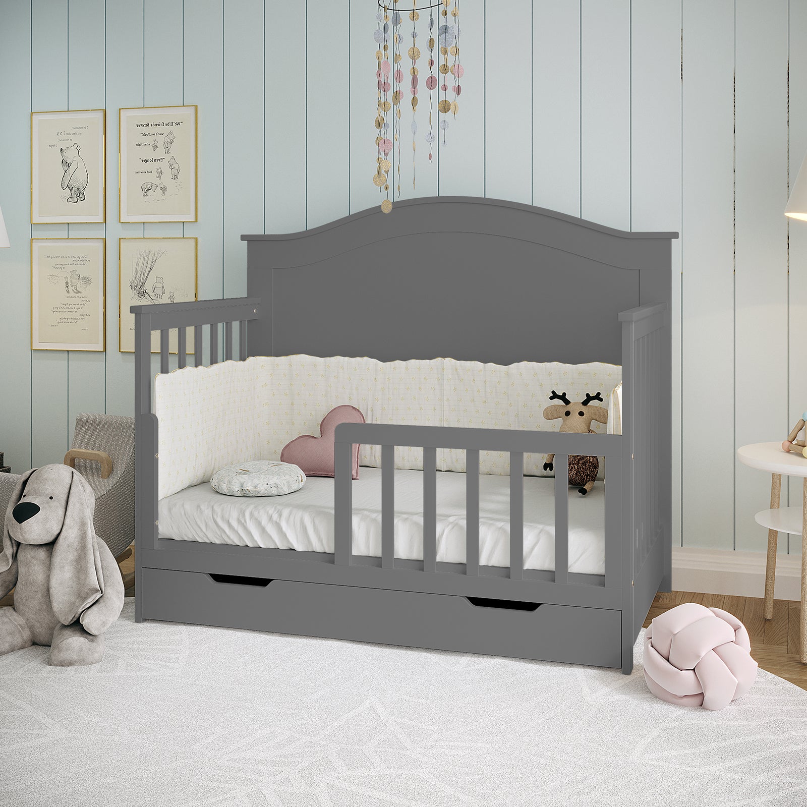 Azeem & Giro Solid Pine Convertible Cot Set in Grey features a slate-gray wooden daybed with padded cream crib bumpers, storage drawer, and decorative pillows, creating a cozy, adaptable nursery space.