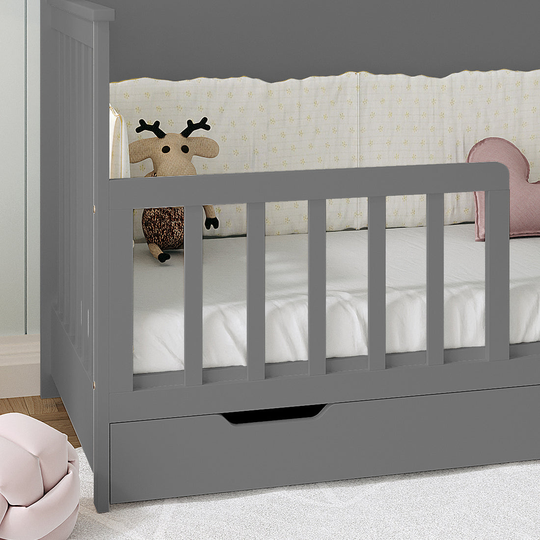 Azeem & Giro Solid Pine Baby Cot with Convertible Rail Set Grey features slatted guardrails, a pull-out drawer, and a knit reindeer plush with a pink heart cushion on the mattress.