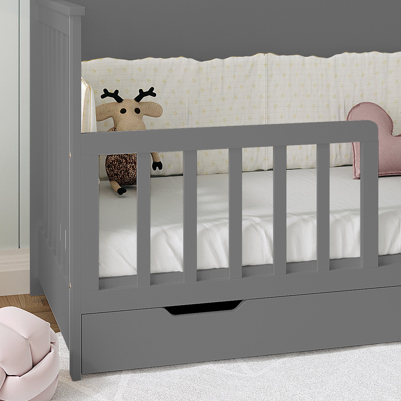 Azeem & Giro Solid Pine Baby Cot with Convertible Rail Set Grey features slatted guardrails, a pull-out drawer, and a knit reindeer plush with a pink heart cushion on the mattress.
