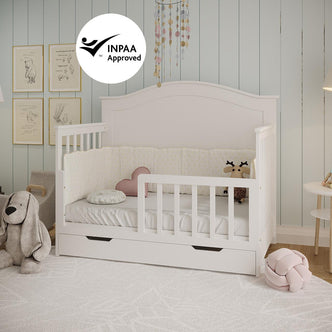 Azeem & Giro Baby Cot with gently arched headboard features a pull-out storage drawer. Includes Gydas 10cm Nursery Mattress, padded bumper, pink cushion, and stuffed reindeer for comfort and security.