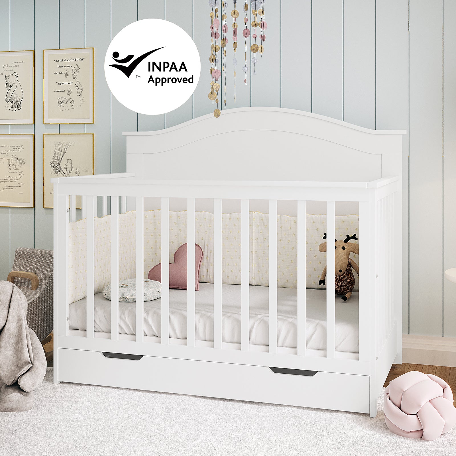 Azeem Baby Cot with slatted sides and storage drawer, paired with Gettel 10cm Nursery Mattress. Features cushions and a stuffed moose toy, under a mobile, creating a serene nursery setting.