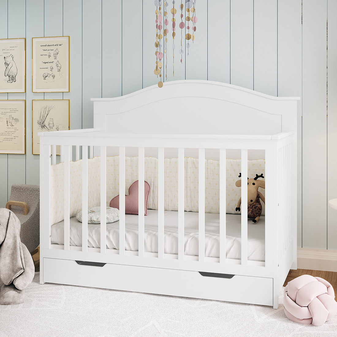 Azeem Baby Cot with Gettel 10cm Nursery Mattress, featuring a star-patterned bumper, cushions, and a plush toy, set against a pale blue paneled wall with a delicate garland above.