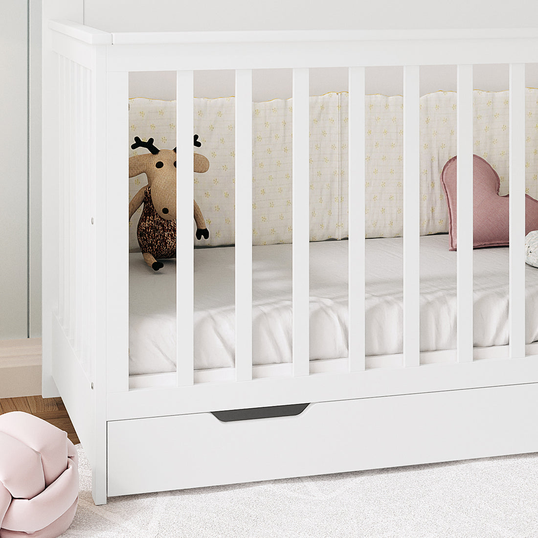 Azeem Baby Cot with slatted sides, featuring a yellow-flower crib bumper, pink heart cushion, and knitted reindeer. Includes pull-out drawer and paired with Gettel 10cm Nursery Mattress for comfort.