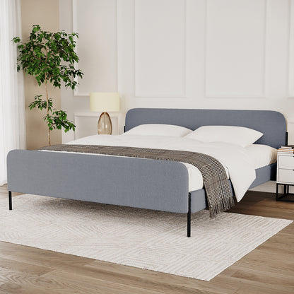 Bonny King Boucle Bed Frame in Grey, featuring muted slate-gray boucle upholstery, slender black metal legs, and a low-profile design, elegantly styled with white linens and a houndstooth throw.