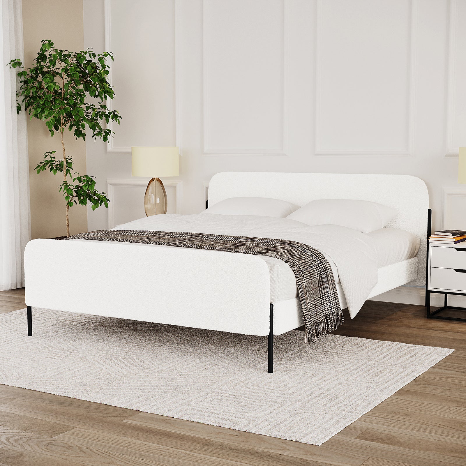 Bonny Queen Boucle Fabric Bed Frame in Cream White with upholstered headboard and footboard, slim black metal legs, and white bedding against a paneled wall, flanked by nightstands and a potted plant.