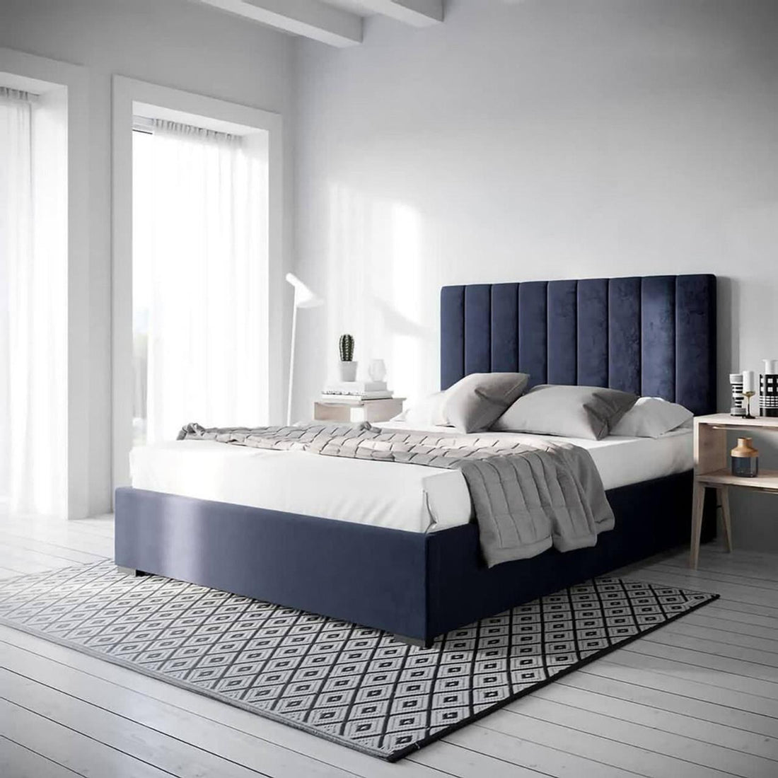 Septima Upholstered Velvet Queen Bed Base in Navy with a blue headboard, featuring elegant velvet fabric and a sturdy wood frame. The bed is complemented by a rug and blanket in a chic interior setting.