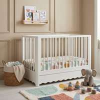 White timber standalone baby cot with a scalloped under-bed trundle drawer.