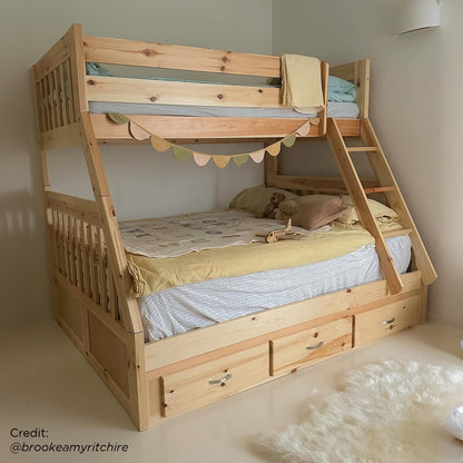 Cornelia Solid Wood Triple Bunk Bed with Storage features a pine structure with a twin over full design, ladder access, guard rails, three storage drawers, and decorative pennant garland.