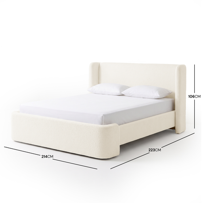 A white bouclé bed frame with a high winged headboard, curved footboard, and white bedding, shown with dimension measurements of 214cm width, 223cm length, and 106cm height on a white background.