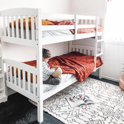 Child sitting on a bunk bed, holding a basket, showcasing the Dante 2-in-1 Solid Pine Timber Bunk Bed – White, highlighting its convertible design and durable pine wood frame.