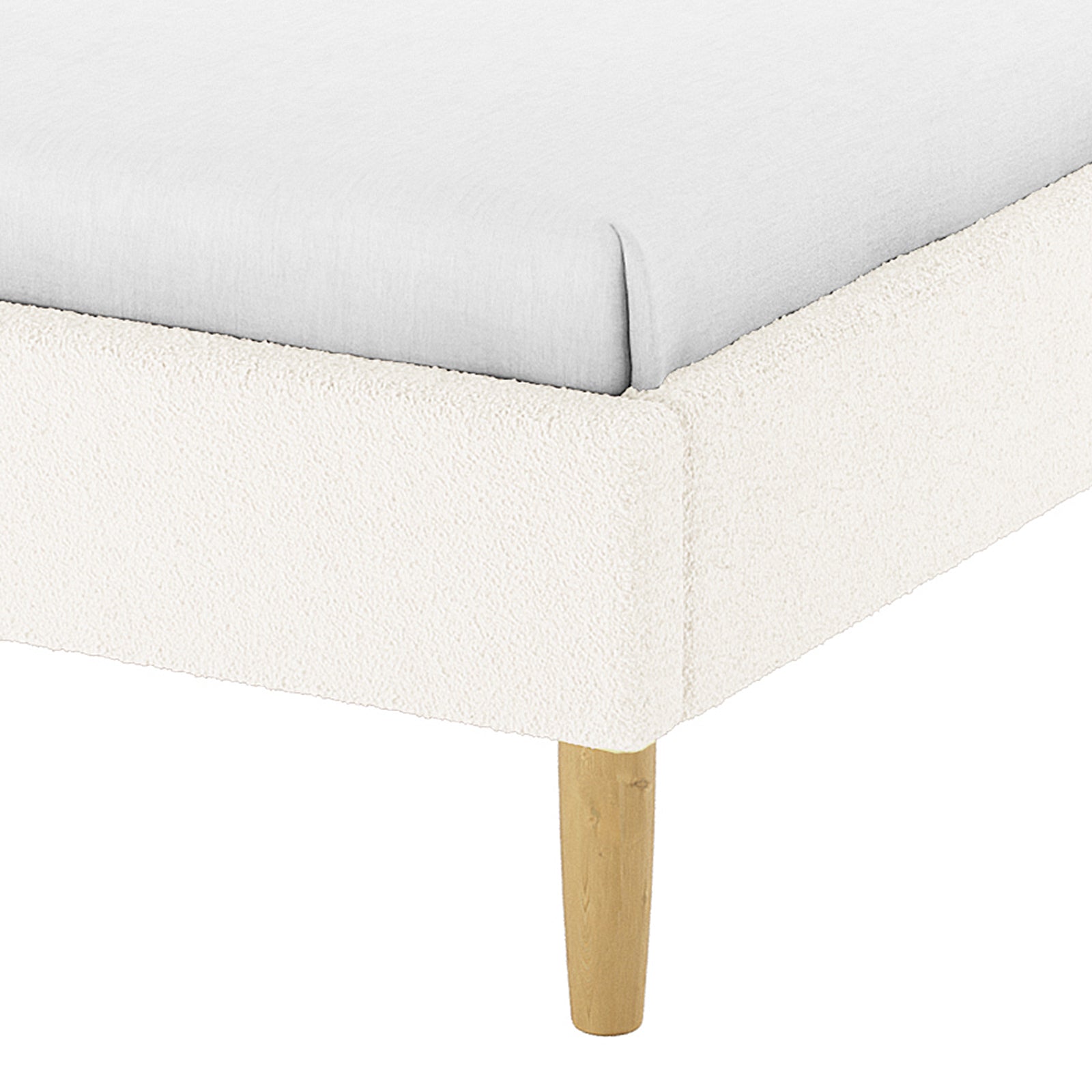 Close-up of the Estilla Double Rainbow Boucle Bed Frame in Cream White, showing a light-colored fitted sheet on the cream-bouclé upholstered platform with a tapered wooden leg for support.