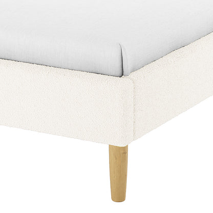 Close-up of the Estilla Double Rainbow Boucle Bed Frame in Cream White, showing a light-colored fitted sheet on the cream-bouclé upholstered platform with a tapered wooden leg for support.