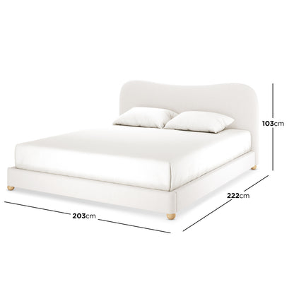 Ginnie Bouclé Curved King Bed Frame – Cream White, showcasing a minimalist design with a curved headboard, upholstered in light-neutral fabric. It features short wooden legs and includes a mattress with two pillows.